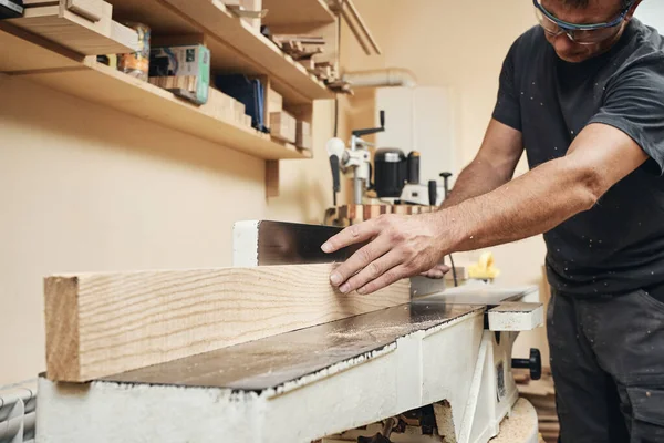 Bir marangoz atölyesindeki öğütme makinesinde çalışır. Tahta levhaların ilk işlemleri.