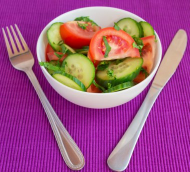 Taze bahar sebze salatası (salatalık, domates) parlak mor arka plan üzerinde beyaz bir kase