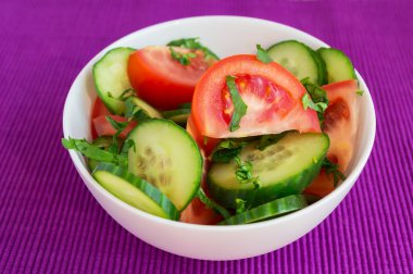 Taze bahar sebze salatası (salatalık, domates) parlak mor arka plan üzerinde beyaz bir kase