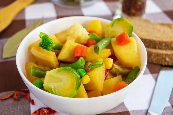 Estofado de verduras (patatas, espárragos, zanahorias, coles de Bruselas, maíz, guisantes, col de col rizada, brócoli) en un tazón blanco. Vegano —  Fotos de Stock