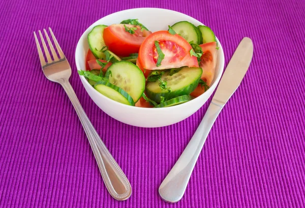 Свіжий весняний овочевий салат (огірки, помідори) у білій мисці на яскраво-фіолетовому фоні — стокове фото