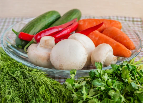 Свежие огурцы, грибы, перец чили, морковь, зелень на круглой прозрачной миске . — стоковое фото