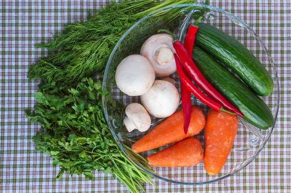 Concombres frais, champignons, piment, carottes, légumes verts dans un bol rond transparent. La vue du dessus . — Photo