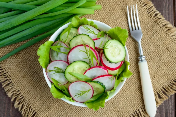 Fresh spring light vegetarian salad with cucumber and radish and greens on a wooden background. — Stock Photo, Image