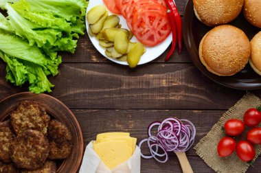 Hamburger (ekmek rulo, domates, salatalık, soğan, marul, domuz eti, peynir) üzerinde ahşap arka plan yapmak için malzemeler