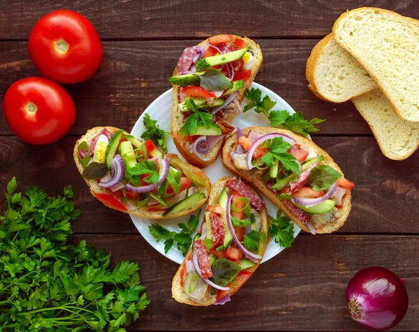 Sendviče s zelení, rajčata, maso, salám na křupavé pečivo na stole — Stock fotografie