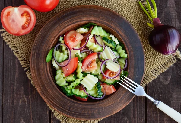 Vitamin salad with cucumbers, tomatoes, purple onion and cheese in a clay bowl on wooden table — Stock Photo, Image