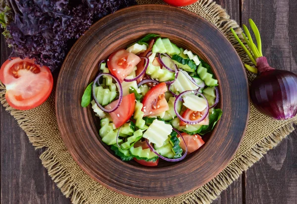 Vitamin salad with cucumbers, tomatoes, purple onion and cheese in a clay bowl on wooden table — Stock Photo, Image