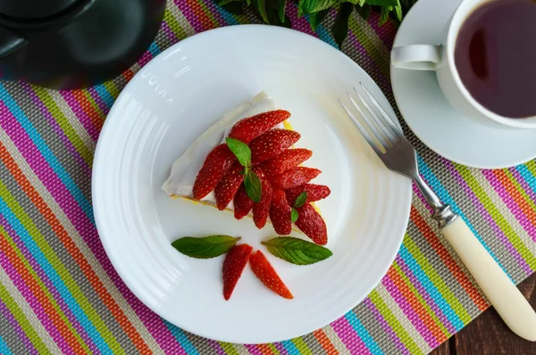 A piece of banana-strawberry sponge cake decorating with mint leaves on a white plate and cup of tea