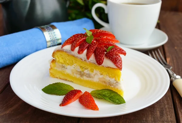 Un pedazo de pastel de esponja de plátano y fresa decorando con hojas de menta en un plato blanco y una taza de té sobre fondo de madera —  Fotos de Stock