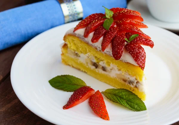 Un pedazo de pastel de esponja de plátano y fresa decorando con hojas de menta en un plato blanco sobre fondo de madera —  Fotos de Stock