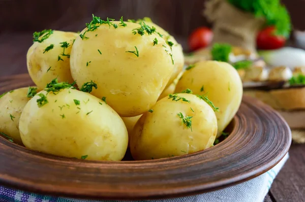 Patatas jóvenes hervidas con mantequilla y eneldo en un tazón de barro sobre un fondo de madera . — Foto de Stock