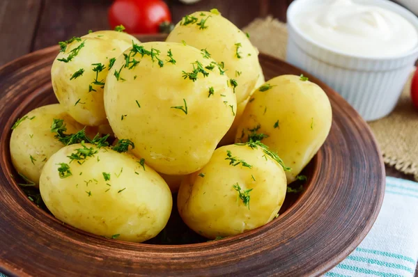 Jovens batatas cozidas com manteiga e endro em uma tigela de barro em um fundo de madeira . — Fotografia de Stock