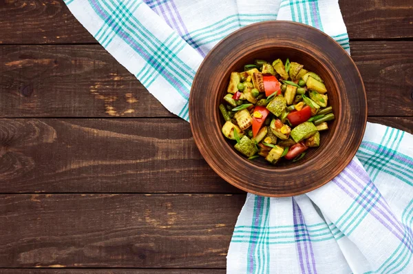 Diätvegetarischer Salat mit gegrillten Zucchini, frischen Tomaten, Mais und Kräutern in einer Tonschale auf dunklem Holzgrund — Stockfoto