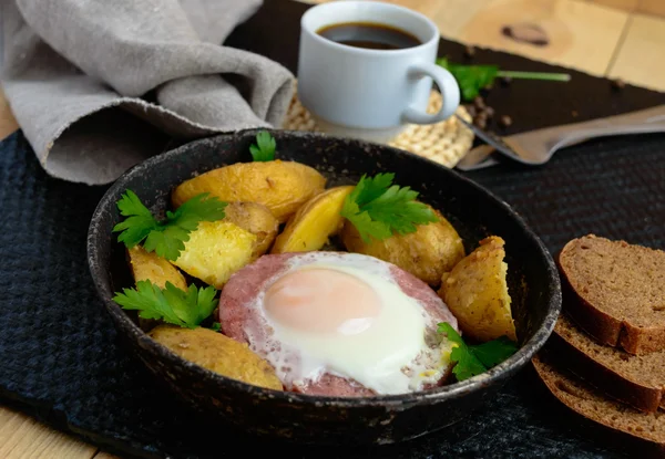 Жареное яйцо в салями и печёная картошка. Подача сковородки с чашкой кофе и ржаным хлебом . — стоковое фото