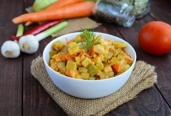 Ragoût végétarien de légumes d'été (courgettes, carottes, tomates, épices, ail, piment) dans un bol blanc sur fond de bois . — Photo