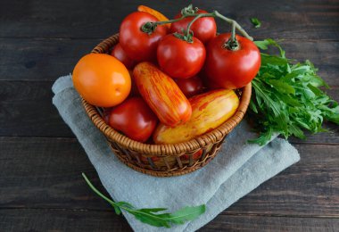 Sepet farklı çeşitleri ve koyu ahşap arka plan üzerinde arugula sheaf domates ile