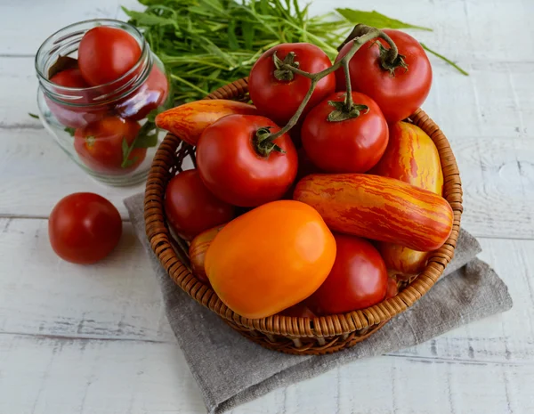 Cesta con tomates de diferentes variedades y gavilla de rúcula sobre fondo de madera blanca — Foto de Stock