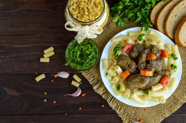 Pasta y hígado de ganso frito (pollo, pato) con pesto y tomate sobre un fondo de madera . — Foto de Stock