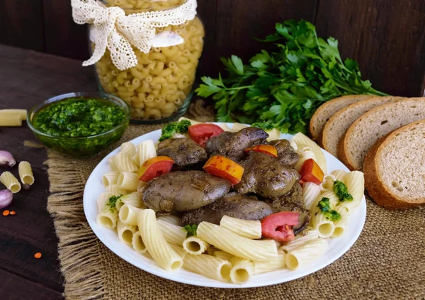 Pasta y hígado de ganso frito (pollo, pato) con pesto y tomate sobre un fondo de madera — Foto de Stock