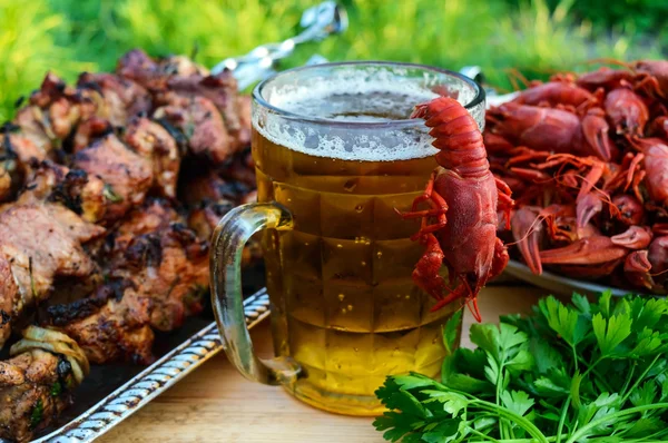 Birra schiumosa in un bicchiere e gamberi bolliti, carne alla griglia su spiedini — Foto Stock