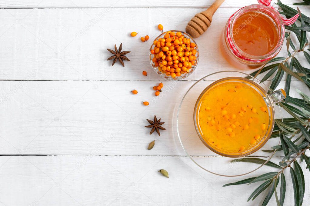 Colorful hot natural sea buckthorn tea in a glass cup, fresh raw berries and leaves, honey, anise and cinnamon sticks. Vitaminic healthy medicine drink. Concept of warm seasonal beverages. Top view, copy space