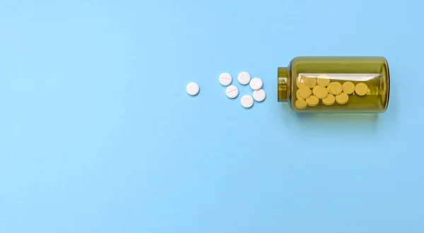 白色圆形药丸分散在蓝色背景的棕色瓶子上 健康药丸 抗生素 维生素 药学和保健主题 医疗背景 顶部的风景 复制空间 — 图库照片