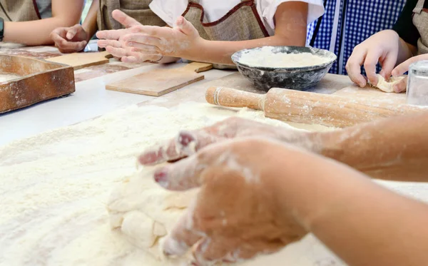 The cook teaches children to making dough. The female hand kneads the dough on a floured table. Master class in baking. Cooking at home.