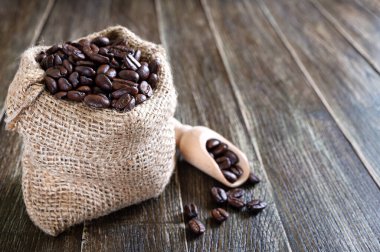 Çuvalda kavrulmuş kahve çekirdekleri ve ahşap bir masaya serpilmiş. Kahve teması, kahvaltı konsepti, enerji, tazelik, kopyalanmış aroma.