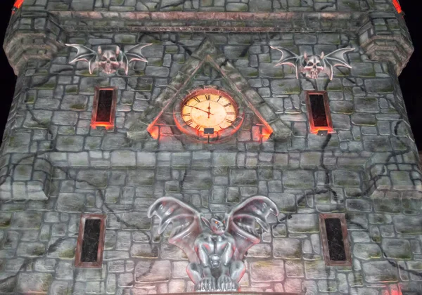 Halloween stone castle with luminous clock and gargoyles. Close-up, bottom view. Installation of the castle of horror.