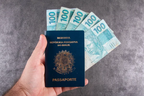 Mão Segurando Passaporte Brasileiro Com Cem Notas Reais — Fotografia de Stock