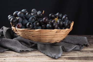 Eski ahşap ve siyah arka planda sepetteki mor meyve üzümü..