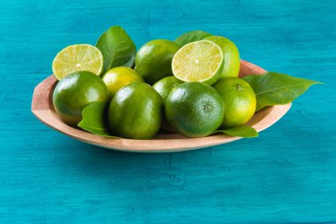 Mavi arka planda ahşap kasede yeşil kireç meyvesi.