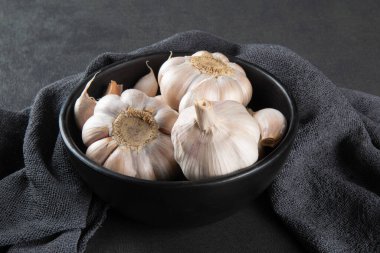 Sarımsak ve soğan siyah kasede kumaş ve koyu arkaplanda..