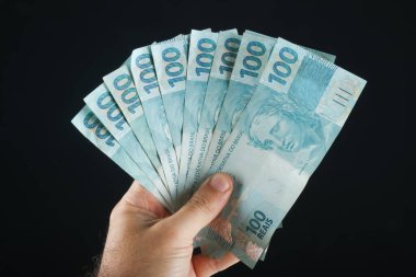 Brezilya parasıyla el ele tutuşmak. 100 reais banknot. Siyah arkaplan.