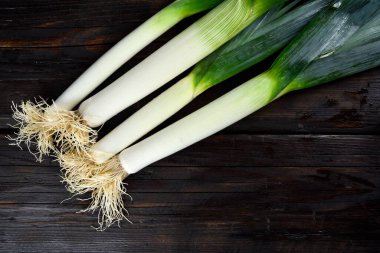 Koyu ahşap arka planı olan taze pırasalar.