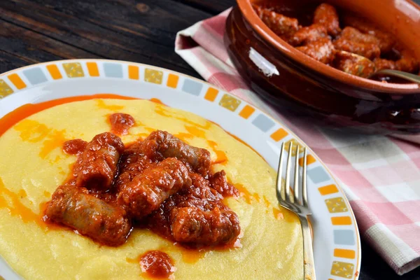 Tabakta polenta ve ahşap bir masada sosis.
