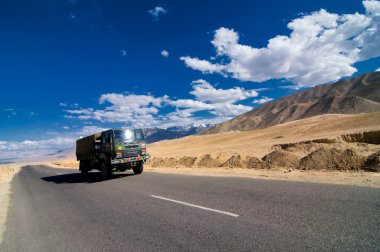 Yüksek dağ dolambaçlı yol çöl manzara ve engebeli dağ duvarı ve Pangong aralığında dramatik bulutlu gökyüzü arka plan karşı bir araba, Ladakh, Himalaya, Jammu & Keşmir, Kuzey Hindistan 