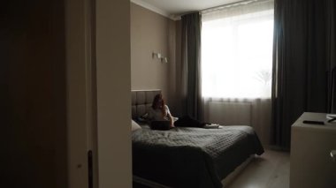 Woman relaxing in a cozy room with a laptop on the bed during daytime