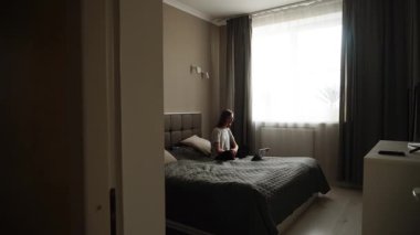 Woman working on laptop in cozy bedroom with natural light in the morning