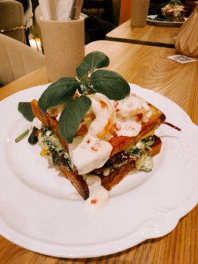 Delicious sandwich stacked high with vegetables, bread, and creamy sauce in a cozy cafe setting