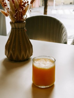 Kurumuş çiçeklerle süslenmiş vazonun yanındaki masada portakal suyunu tazeliyorum.