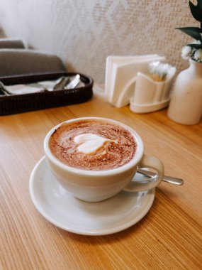 Sıcak bir fincan cappuccino, rahat kafe ortamında, ahşap masada.