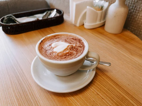 Warm cup of creamy coffee placed on a wooden table in a cozy cafe setting
