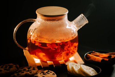 Warm black tea served in a glass teapot with cookies and lemon slices at home