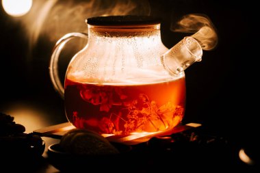 Hot black tea brewing in a pot with steam rising in a cozy setting