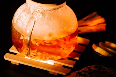 Warm black tea brewing with flowers on a wooden tray by candlelight in the evening