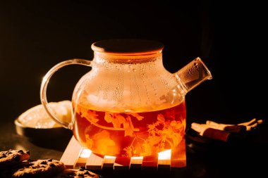 Enjoying a warm pot of black tea with cookies in a cozy setting during evening hours