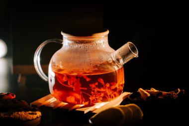 Brewing black tea in a glass pot with herbs and spices in a cozy setting