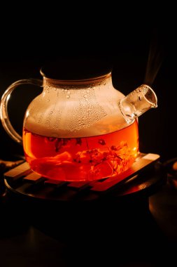 Warm black tea brewing in a glass teapot with steam rising in a cozy setting